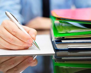 businessman is writing on document and a lot of documentation is waiting to be reviewed