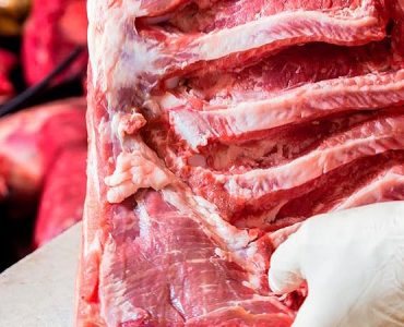 Butcher woman cutting piece of rib meat in her shop with a knife